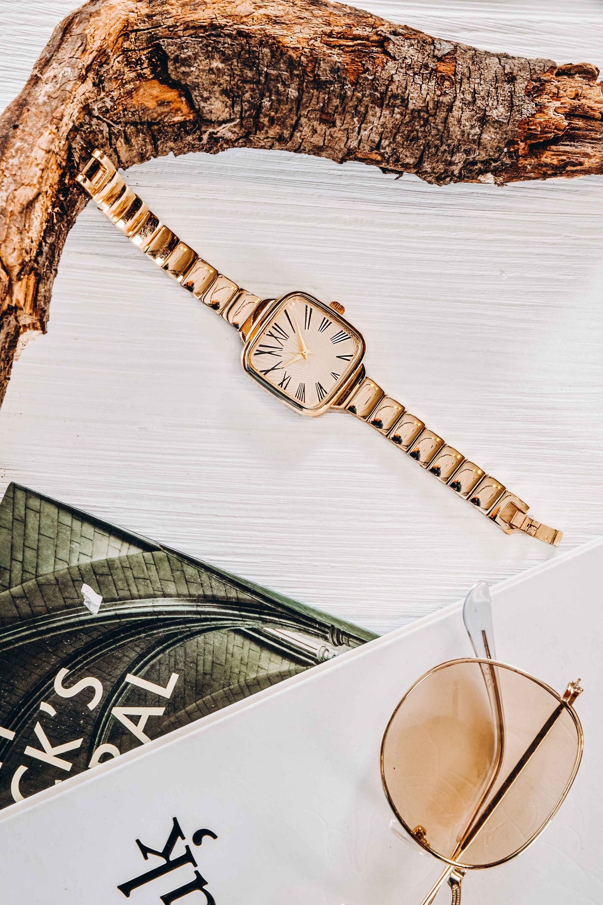 Gold wristwatch, sunglasses and a book in a flat lay - accessories to pair with a men's co-ord set