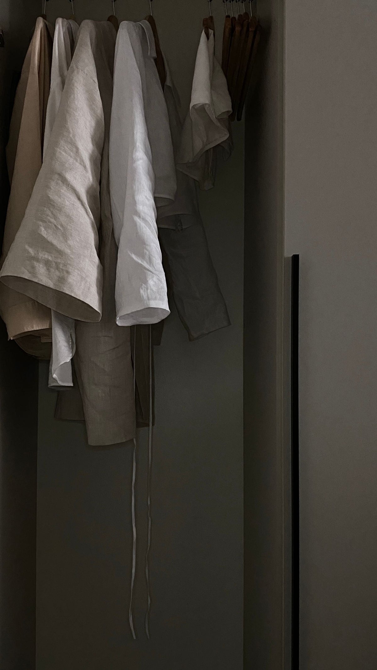 Neutral linen shirts and trousers hanging separately in a closet, illustrating mix-and-match wardrobe pieces