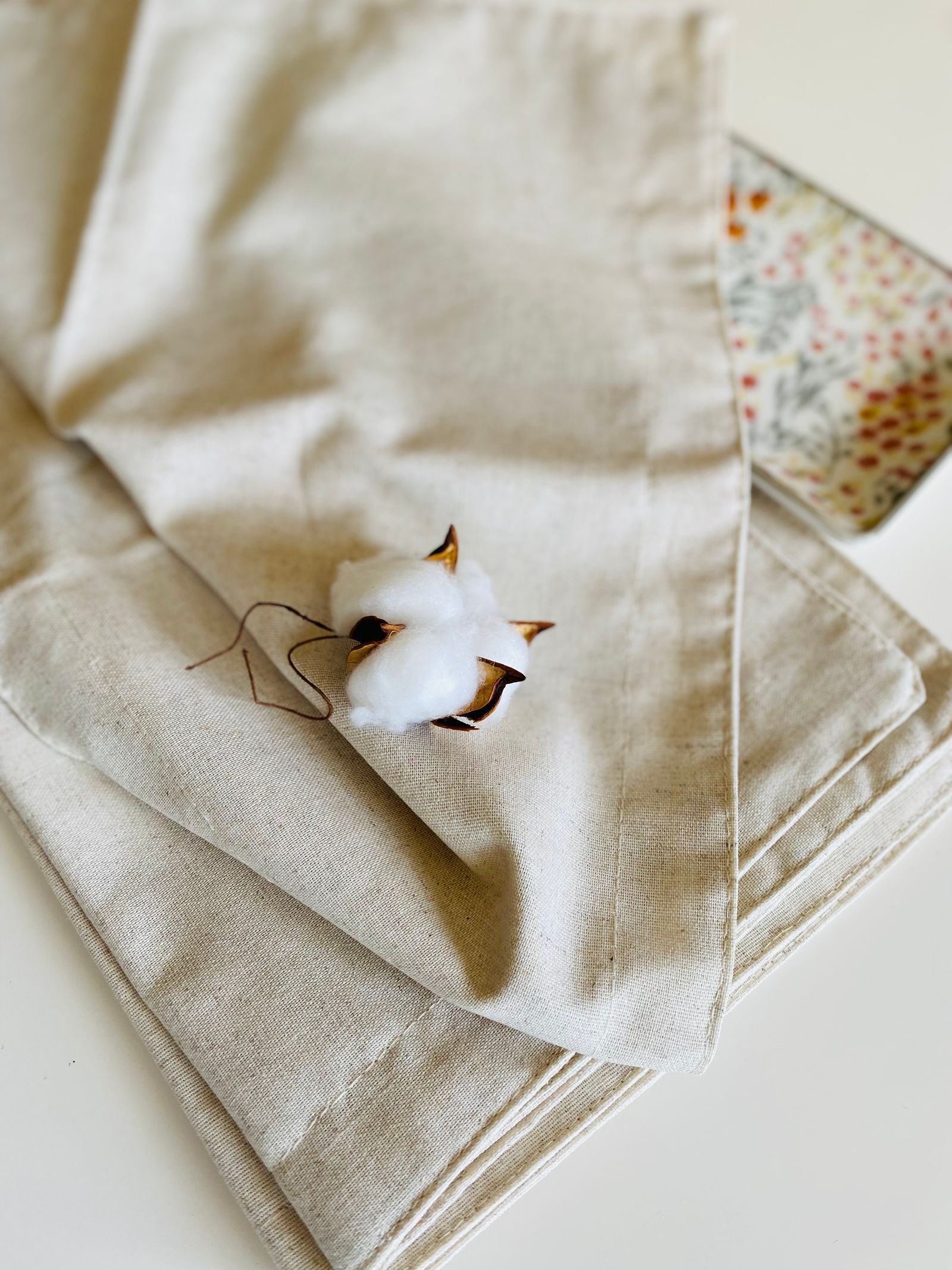 Cotton boll resting on beige linen fabric - linen vs cotton for Indian summers